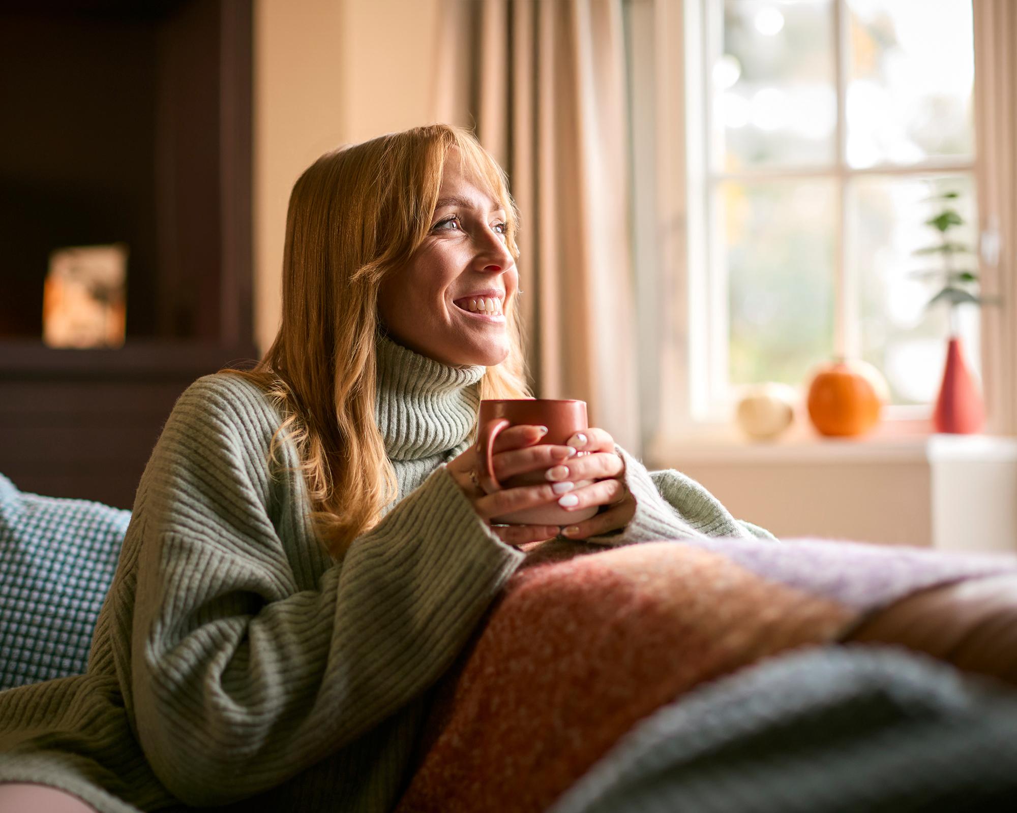 Frau sitzt auf Sofa mit Tasse in der Hand